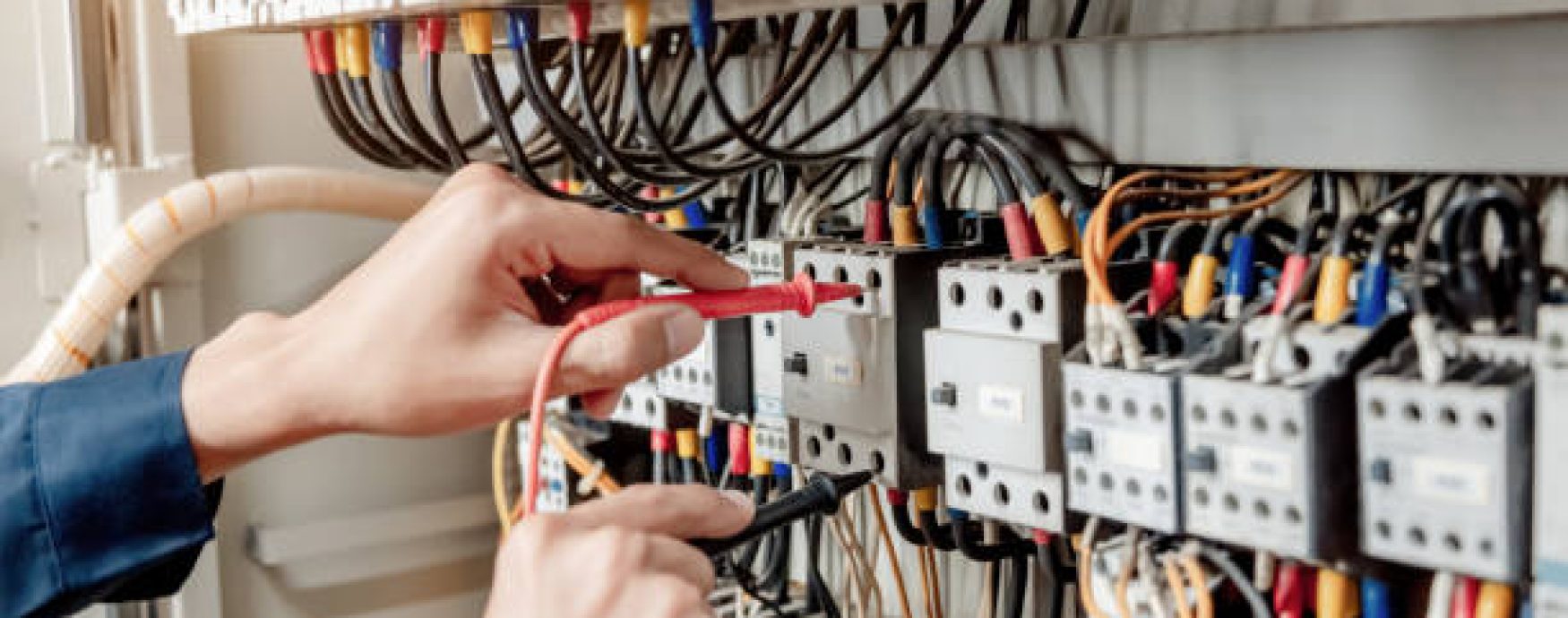 Electrician engineer uses a multimeter to test the electrical installation and power line current in an electrical system control cabinet.
